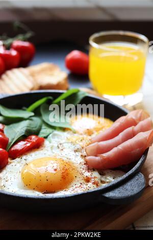 Deliziose uova fritte con spinaci, pomodori e prosciutto serviti sul tavolo Foto Stock