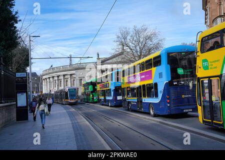 Strada trafficata a Dublino con autobus e tram, che conduce a Piazza del Parlamento a College Green Foto Stock