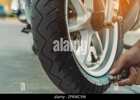 Mani di un uomo controllare la pressione del generatore di gas e gonfiare uno pneumatico su una motocicletta con un compressore pneumatico. Man controllo della pressione dell'aria e riempimento della pressione dei pneumatici Foto Stock