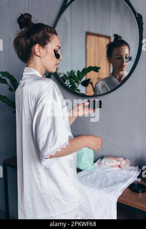 Giovane donna che tiene il vaso con le zone, applicante sul suo viso. Foto Stock