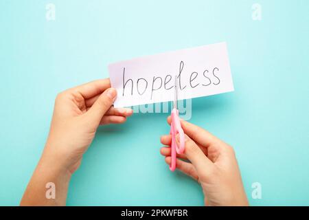 Le mani della donna tengono una carta con la parola senza speranza, tagliala con le forbici per fare speranza. Vista dall'alto Foto Stock