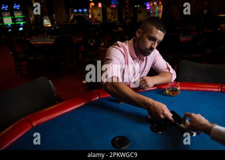 Giovane uomo che gioca a Blackjack dietro al tavolo al Casinò Foto Stock