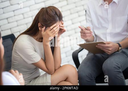 Giovane donna d'affari frustrata e infelice tenendo testa in mano alla sessione di psicoterapia, psichiatra facendo appunti diario in ufficio Foto Stock