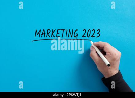 La mano maschile sottolinea la parola Marketing 2023 su sfondo blu. Strategie e piani commerciali di marketing per l'anno 2023. Foto Stock