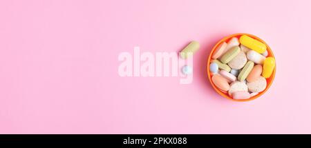 Pillole colorate, capsule, vitamine e integratori alimentari di diversa forma, dimensione e colore in una ciotola isolata su sfondo rosa. Banner Web. Foto Stock