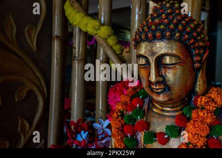 Primo piano della statua di buddha di bronzo seduta in meditazione con decorazioni floreali per la cerimonia del festival. Foto di alta qualità Foto Stock