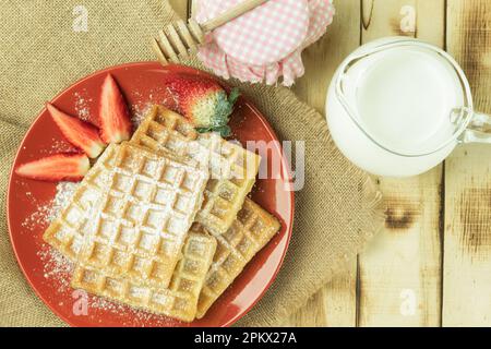 Waffle belgi freschi con frutta, vista dall'alto. Colazione gustosa. Waffle fatti in casa con fragole, zucchero a velo su un piatto, su uno sfondo di legno. S Foto Stock