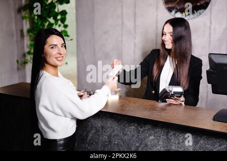 Un giovane e cordiale portiere si trova dietro un banco del ricevimento e fornisce informazioni sulle camere agli ospiti che effettuano il check in in un hotel. Foto Stock