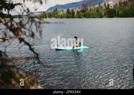 Uomo che pesca in kayak su un lago in montagna con il cane Foto Stock