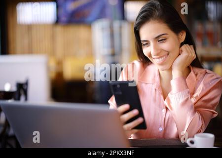 Donna freelance felice che utilizza più dispositivi seduti in un bar Foto Stock