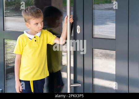 Un ragazzo un po' sconvolto che tiene la maniglia della porta non può aprire la porta. Il bambino ritorna a casa. Foto Stock