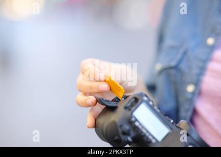 Primo piano di una mano fotografa che instauna scheda sd sulla fotocamera in strada Foto Stock