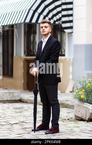 L'uomo europeo in tuta è in piedi con un ombrello per strada Foto Stock