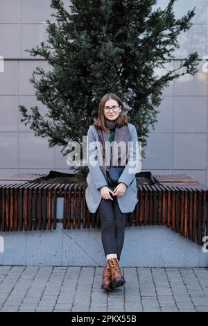 donna dai capelli castani in occhiali che indossa un cappotto e una sciarpa in autunno Foto Stock