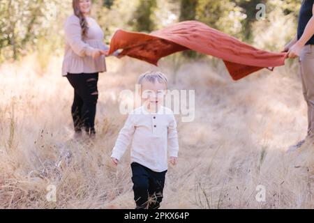 Adorabile bambino che corre sotto coperta mamma e papà tenendo Foto Stock