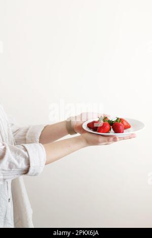 donna cuoco tiene in mano un piatto con fragole fresche rosse Foto Stock