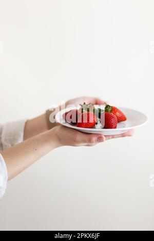 donna cuoco tiene in mano un piatto con fragole fresche rosse Foto Stock