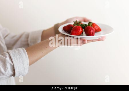 donna cuoco tiene in mano un piatto con fragole fresche rosse Foto Stock
