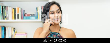 Bella messicana donna adulto maturo che parla al telefono al chiuso a casa Foto Stock