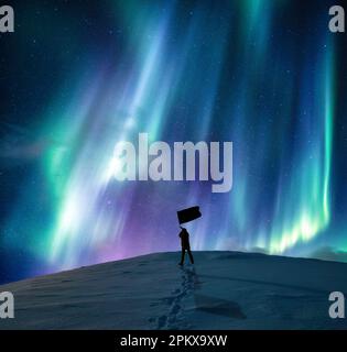 Fantastica aurora borealis, aurora boreale su silhouette uomo felice in piedi bandiera ondeggiante su montagna innevata in cerchio artico in inverno in Norvegia Foto Stock