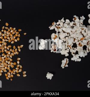 Due mucchi di popcorn, un mucchio di popcorn già pronti, un altro con semi di mais, popcorn su sfondo nero, popcorn per guardare la televisione. Foto Stock