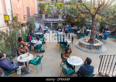 Barcellona, Spagna - 13 marzo 2023: Persone sedute fuori al bar in una piccola piazza. Edifici tradizionali e albero decorativo Foto Stock