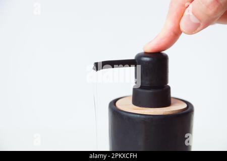 Spruzzi di sapone liquido dal dispenser nero su sfondo bianco. uomo che preme il pulsante del flacone. Foto Stock