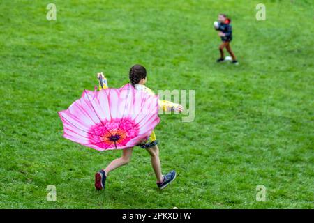 Preston Lancashire. Meteo nel Regno Unito. 10 aprile 2023. Giovane ragazza gioiosa in cima gialla con un ombrello rosa a petalo al tradizionale lunedì di Pasqua che arrotola le uova nel Parco Avenuam, una tradizione che risale al 1867. I bambini rotolano le loro uova di passo giù le colline e vedono chi potrebbe ottenere loro il più lontano senza rompersi. Credit MediaWorldmages/AlamyLiveNews Foto Stock