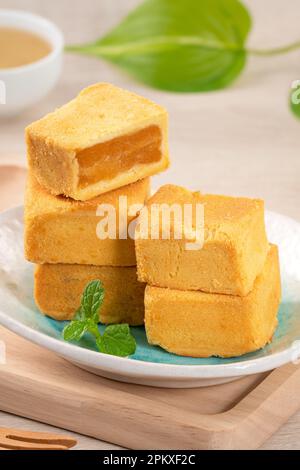 Delizioso dessert taiwanese con torta di ananas in un piatto su sfondo tavolo di legno con tè caldo. Foto Stock
