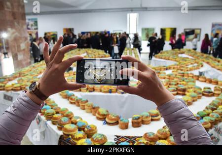 Una donna scatta una foto del Tridente dell'Ucraina da mille dolci pasquali sul suo cellulare. A Lviv, è stato stabilito un nuovo record ucraino - in 25 minuti e 17 secondi, la gente ha decorato 1.000 torte di Pasqua e li ha disposti a forma di tridente. Questo è il più grande tridente ucraino mai fatto da dolci di Pasqua. Tutte le torte di Pasqua saranno vendute, e i proventi saranno utilizzati per acquistare droni per l'esercito ucraino. Foto Stock