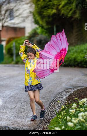 Preston Lancashire. Meteo nel Regno Unito. 10 aprile 2023. Allegra giovane ragazza in cima gialla con ombrello petalo rosa in una giornata piovosa nel centro della città. Oggi un mix di sole e docce soffocanti per la maggior parte, alcuni dei quali possono essere pesanti, con la possibilità di grandine e tuoni. Credit; MediaWorldImages/AlamyLiveNews Foto Stock