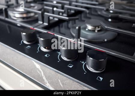 Manopole di controllo con accensione automatica fuoco selettivo closeup su fuori fuoco vetro nero temperato stufa a gas piano cottura con wok bruciatore incorporato compatto Foto Stock