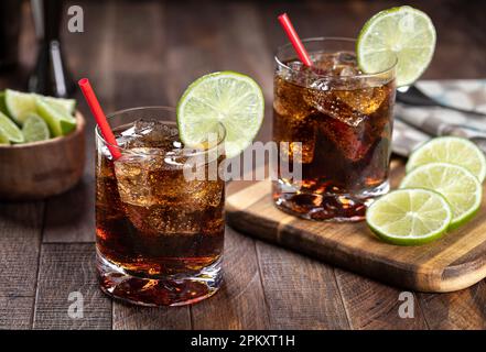 Cocktail al rum e alla cola con fettina di lime su un tavolo rustico in legno Foto Stock