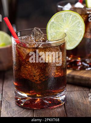 Cocktail al rum e alla cola con fettina di lime su un tavolo rustico in legno. Primo piano Foto Stock