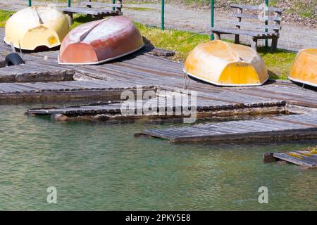 Fatiscente molo in legno abbandonato con vecchie barche a remi colorate rovesciate che giacciono sul lago come concetto per il declino della recessione e del decadimento del turismo Foto Stock