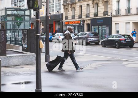 Un uomo nero trascina una borsa su ruote in una strada di Parigi Foto Stock
