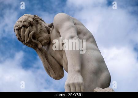Statua in pietra bianca dell'uomo muscoloso con mano sul viso, contro cielo blu e nuvole Foto Stock
