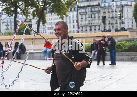 L'uomo crea bolle gioiose con due bastoncini e corda, sorridendo e divertendosi Foto Stock