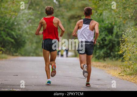 due atleti runner che corrono insieme in park road, maratona autunnale, foglie gialle cadute a terra Foto Stock