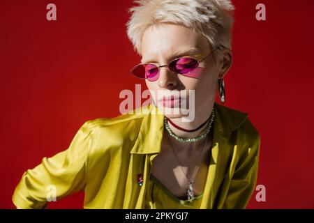 luce del sole sulla faccia del modello albino in occhiali da sole eleganti su sfondo rosa carminio Foto Stock