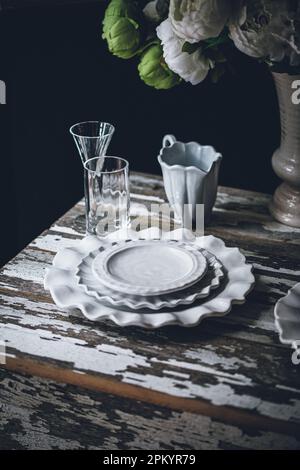 Lastre bianche in ceramica poste vicino alla vetreria e bouquet di fiori freschi su un tavolo di legno scablato Foto Stock