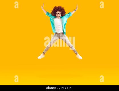 Felice ragazzo divertente in abiti casual e curly parrucca saltando e volando su sfondo di colore giallo Foto Stock