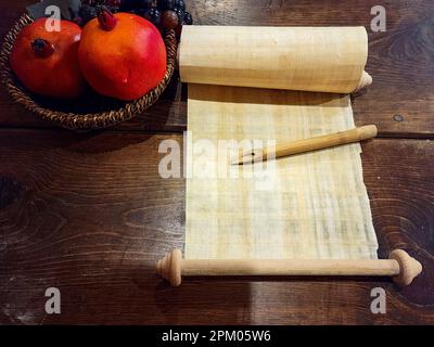 Penna a canna di bambù su un antico rotolo bianco di papiro con frutta di melograno in una vecchia ciotola su un tavolo di legno Foto Stock