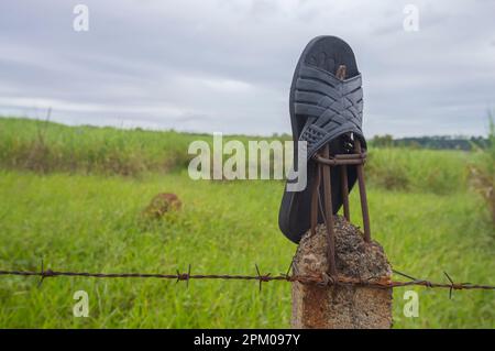 Slipper lasciato su una recinzione con vegetazione in background in una giornata nuvolosa, concetto di inquinamento della natura. Foto Stock