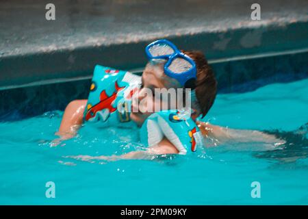 Un ragazzino che gioca in una piscina coperta indossando occhiali e galleggianti a Beckley West Virginia Foto Stock