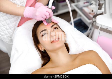 Idro-dermoabrasione, procedura estetica, servizio di cura della pelle, procedura cosmetologica, cosmetologo sta eseguendo una procedura sul volto di una giovane donna sorridente Foto Stock