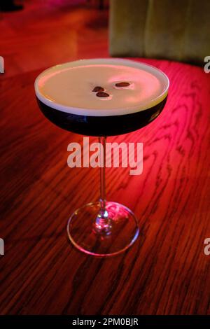 Cocktail russo nero in un classico cocktail bar su un tavolo da bar con luce rossa sullo sfondo Foto Stock