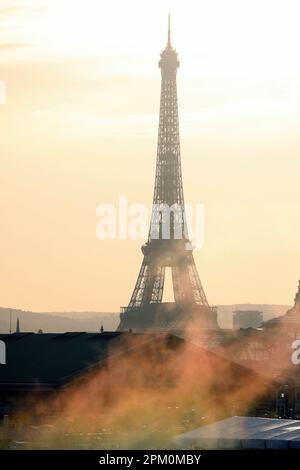 Un tramonto maestoso proietta le sue calde tonalità sulla Torre Eiffel, mentre bagliori di fumo multicolore emanano da un camino in primo piano Foto Stock