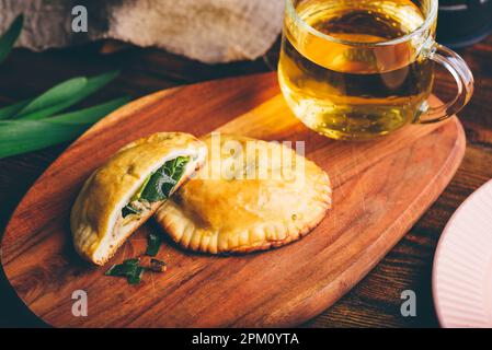 Dolci al forno ripieni di erba cipollina siberiana e funghi con tazza di tè verde su vassoio di legno Foto Stock