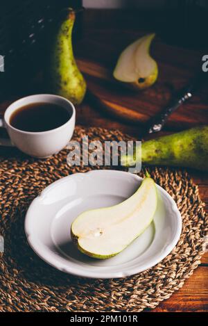 Metà della pera verde sul piatto bianco e tazza di Caffè Foto Stock